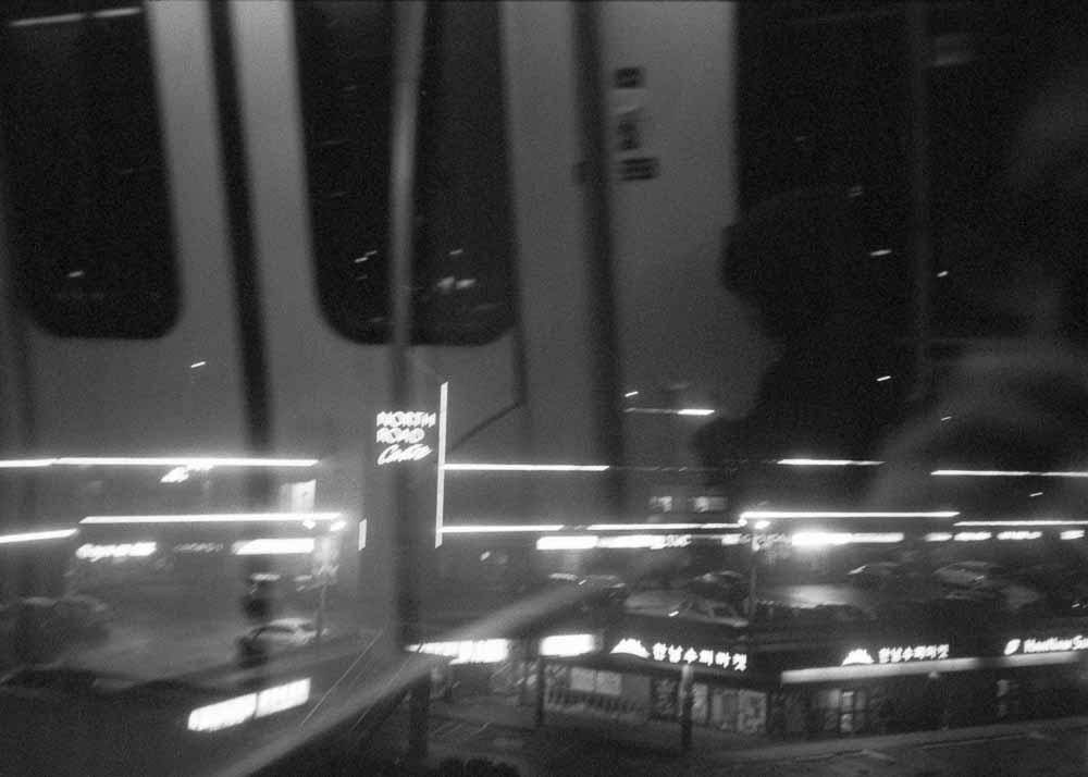 Night. Horizontal stripes of light and the sign for North Road Centre. The train doors reflected in the window.