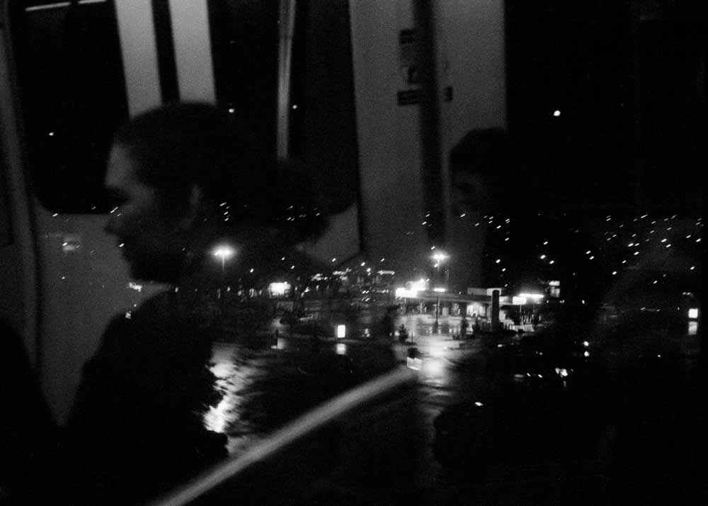 Night. Specks of light, a blurry gas station. Reflected: a woman in profile, facing to the left.