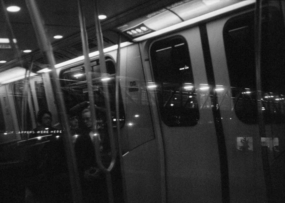 Night. Round lamps and geometric girders. Reflected: round lamps, curving handholds, and a backlit panel above the doors.