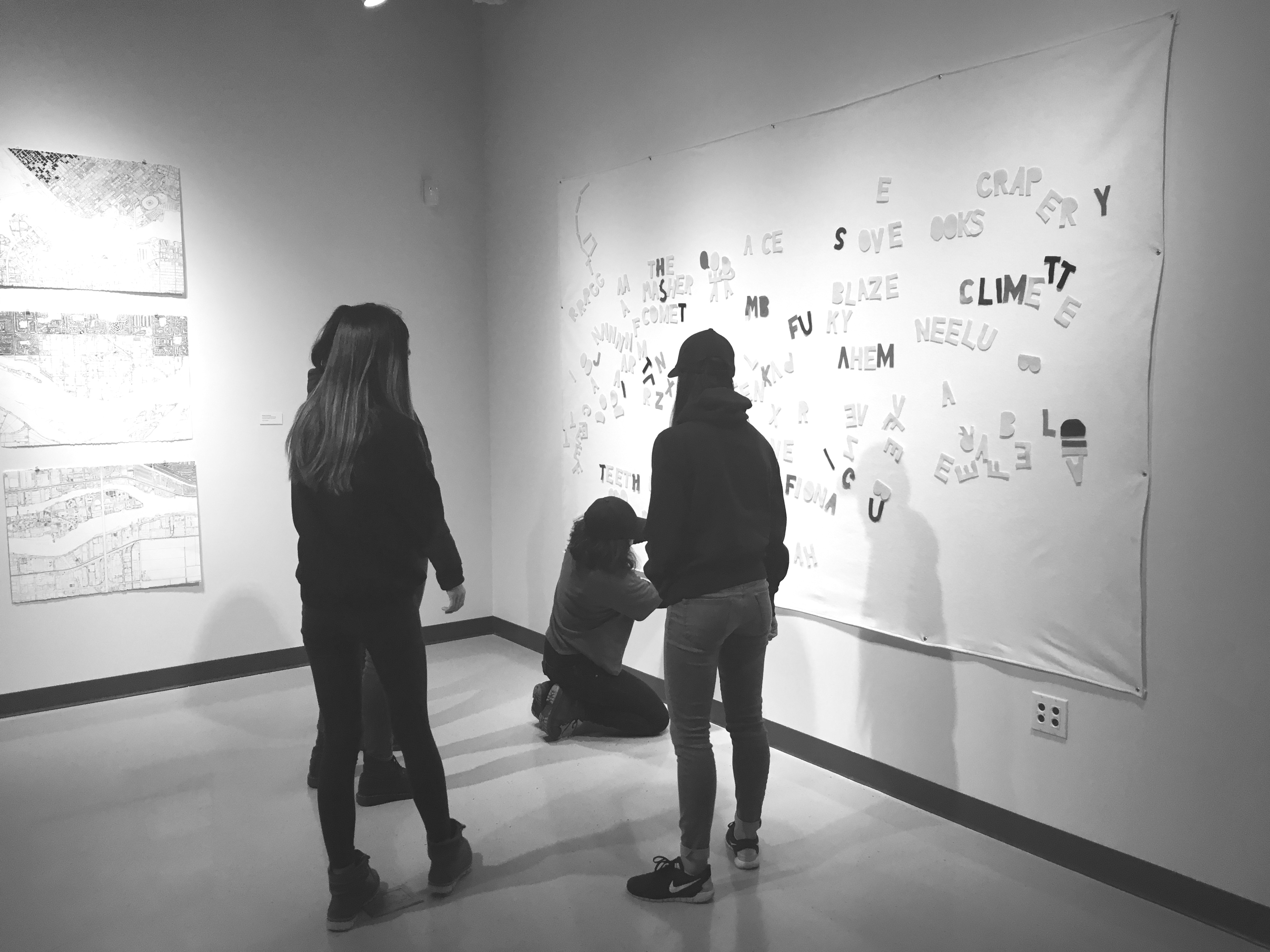 Several people looking at the felt board. One kneels down to arrange letters near the bottom.